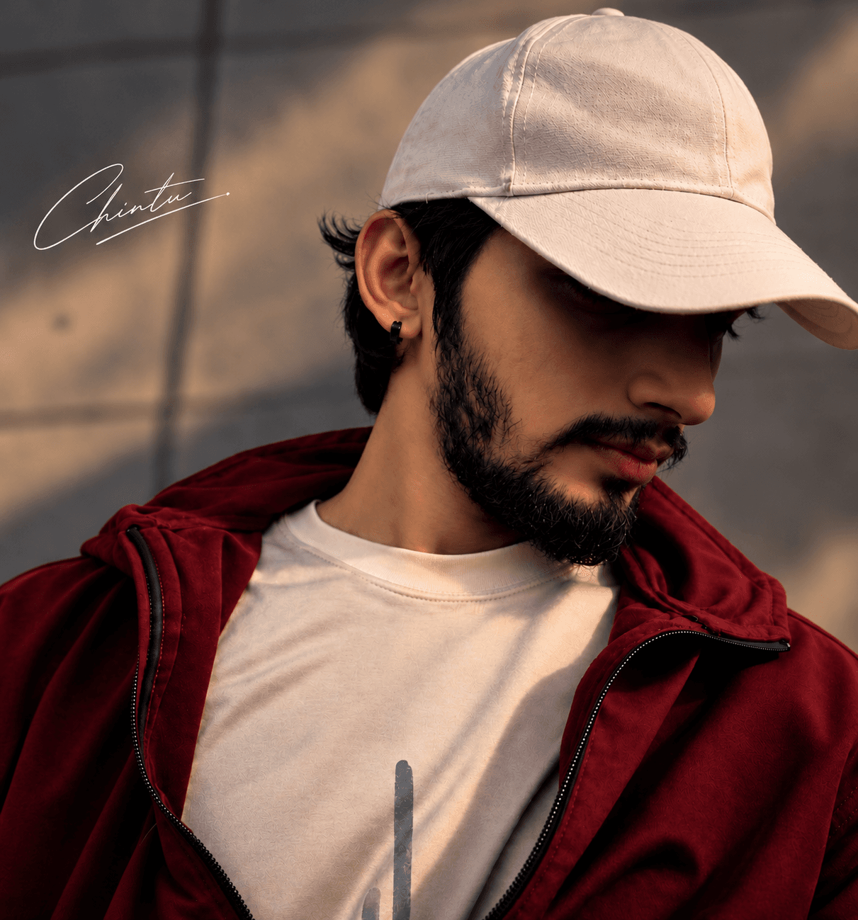 Signed portrait of Bukya Naresh — golden-hour light, white cap, maroon hoodie, Chintu signature
